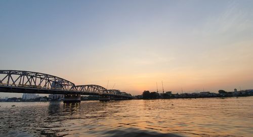 Silhouette bridge over river against sky during sunset