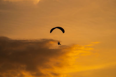 Low angle view of person paragliding against orange sky