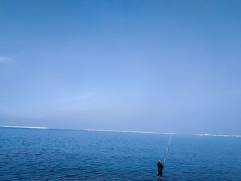 Man fishing in sea against blue sky