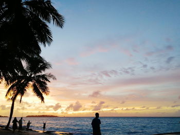 Silhouette people on beach against sky during sunset