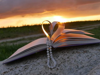 Book pages with beads making heart shape on rock during sunset