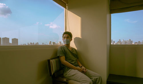 Man sitting by window against sky