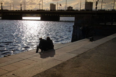 Rear view of people sitting on bridge over river