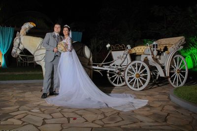 Newlywed couple standing by horse cart against sky at night