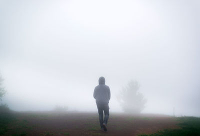 Rear view of man standing on field against sky