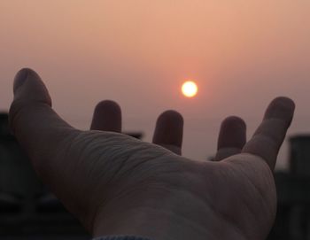 Close-up of hands against sky during sunset