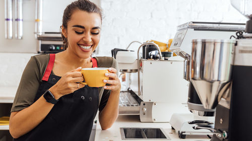 Smiling barista holding coffee cup standing in kitchen at cafe