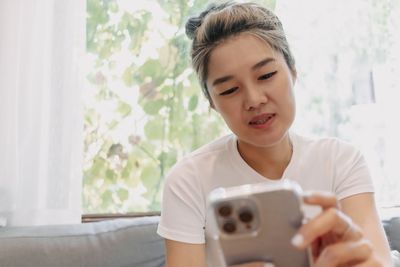 Young woman using mobile phone while sitting on bed at home