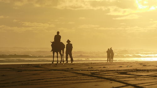 Silhouette people on beach against sky during sunset