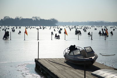 People riding sleds on frozen lake against sky