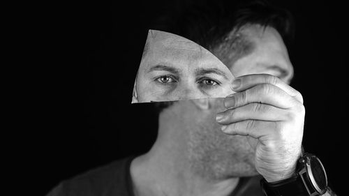 Portrait of man holding mirror piece over black background