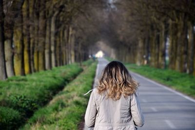 Rear view of woman standing by road against trees