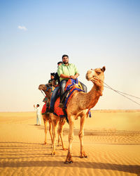 Full length of man riding horse on sand against sky