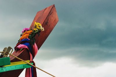 Close- up of flowers tied on longtail boat against cloudy sky