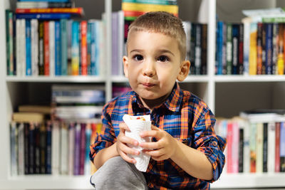Portrait of boy eating snack against bookshelf