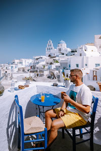 Man sitting on chair against buildings and sky