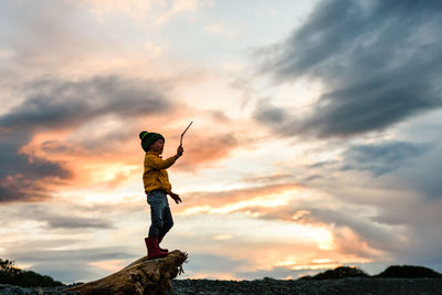 Silhouette of young child holding a stick in the air at sunset