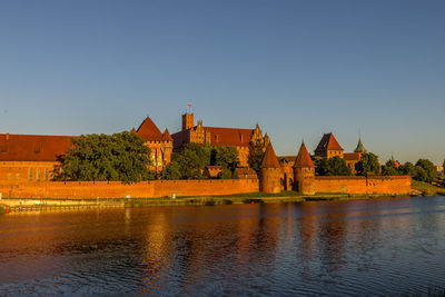 Buildings by lake against clear blue sky