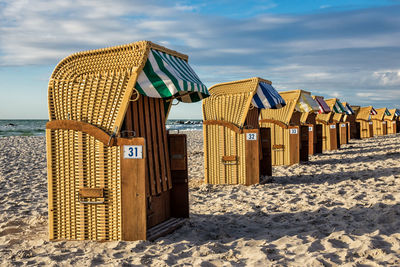 Hooded chairs on beach against sky