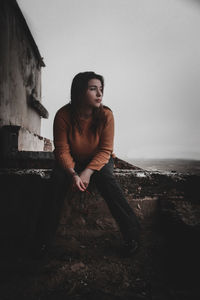Young woman looking away while sitting against sky