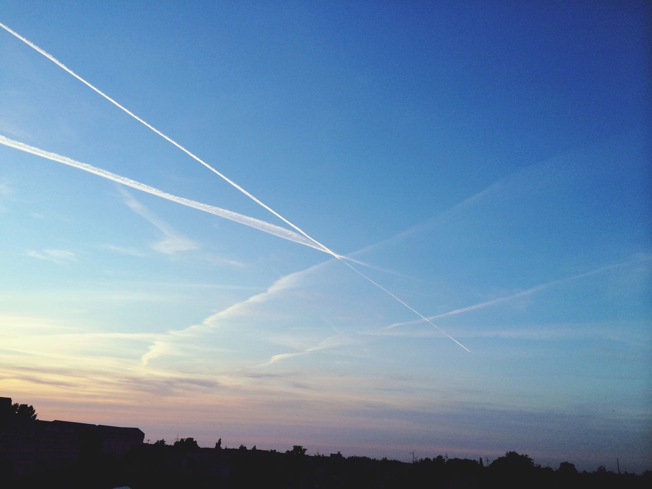 blue, vapor trail, sky, silhouette, built structure, low angle view, building exterior, architecture, city, copy space, scenics, beauty in nature, nature, outdoors, no people, sunlight, clear sky, tranquility, cloud - sky, sunset