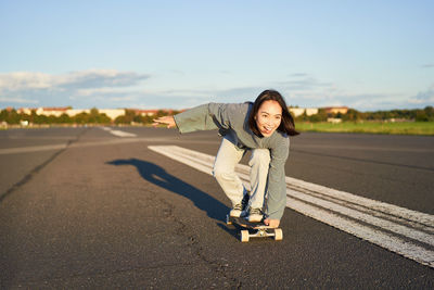 Portrait of young woman standing on road against sky