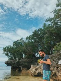 Young man drinking coconut water while standing at beach