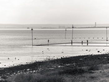 Monochrome people in the distance paddling in a sea pool, shoeburyness