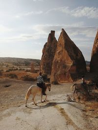 People riding horses on dirt road against rock formations