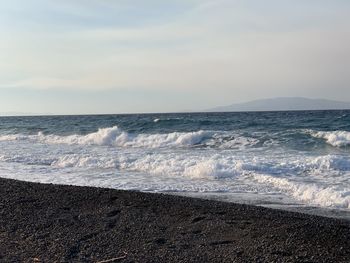 Waves rushing towards shore against sky