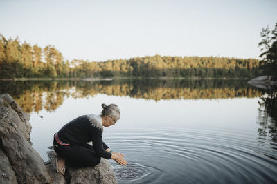 Senior woman crouching on rock at lakeshore