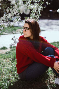 Young woman looking away while sitting on tree