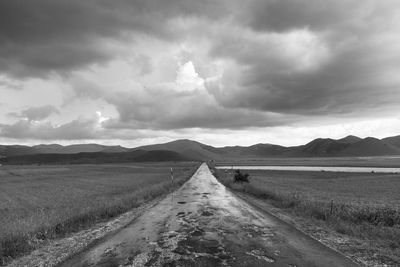 Empty road amidst field against sky