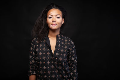 Portrait of young woman standing against black background