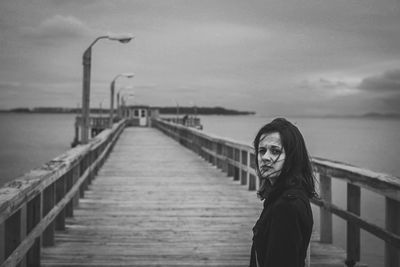 Portrait of young woman standing on bridge over sea against sky