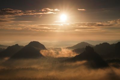 Autumn sunset view over forest to fall colorful valley full of dense mist colred with hot sun rays