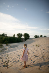 Rear view of girl standing at beach against sky