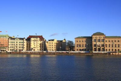 View of buildings by river against blue sky