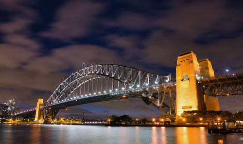 Illuminated bridge over river with city in background