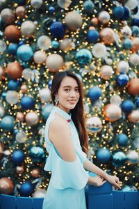 Portrait of smiling young woman standing by christmas tree outdoors