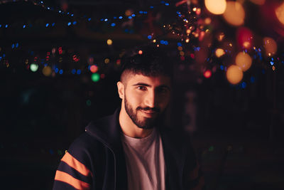 Portrait of smiling bearded man against illuminated colorful lights at bar