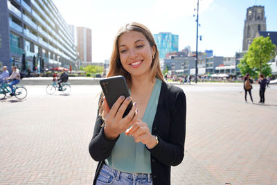 Multi ethnic young woman using smartphone app in rotterdam modern city square, netherlands