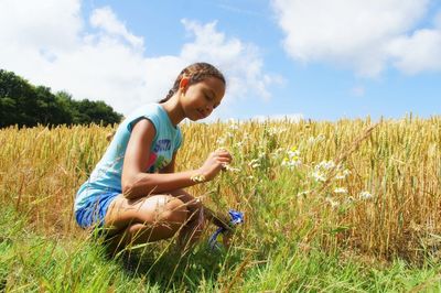 Young woman crouching on grassy field against sky