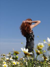 Side view of young woman standing on field against blue sky during sunny day