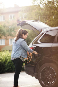 Side view of woman charging electric car on driveway