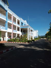 Road by buildings against clear blue sky