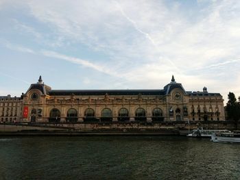 View of building by river against cloudy sky