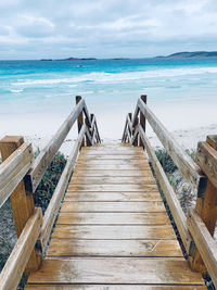 Wooden boardwalk leading towards sea against sky