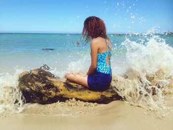 Waves splashing on woman sitting on tree trunk at beach