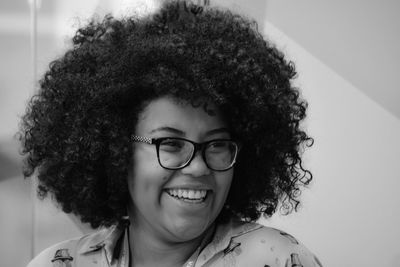 Close-up of smiling woman with curly hair wearing eyeglasses at home